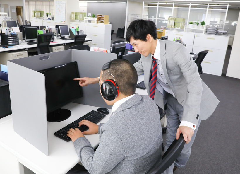 ヘッドフォンをしてパソコンを作業している男性とパソコンを指さしている男性
