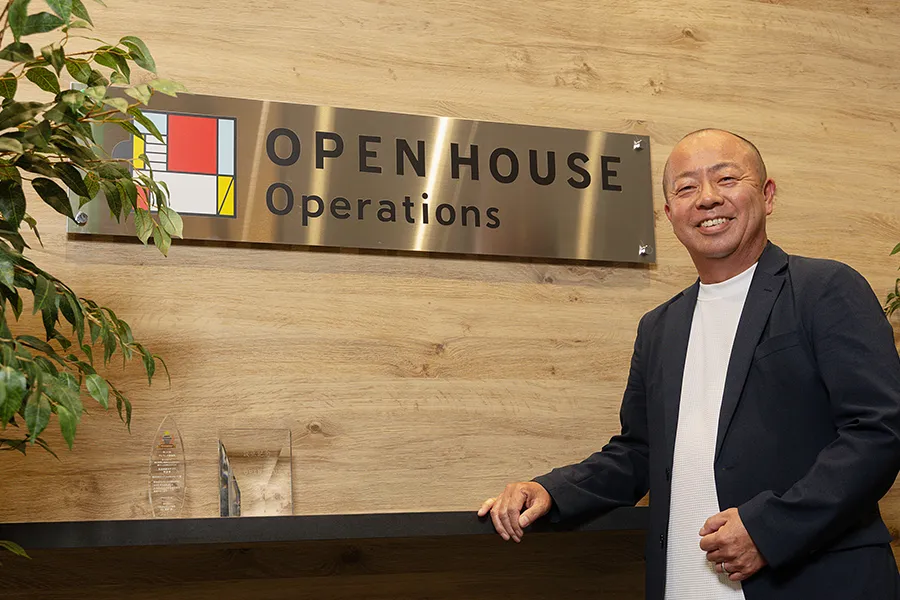 社名プレートの前に笑顔で立っている市川氏